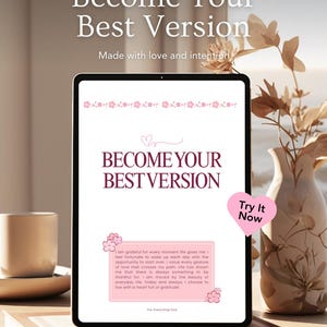 以下が含まれることがあります： デジタルタブレットには、テキスト「Become Your Best Version」と花の装飾が表示されています。画面には、インスピレーションを与えるテキストと「Try It Now」ボタンを備えたピンク色のデザインが表示されています。背景には、ドライフラワーが入った花瓶とコーヒーカップがあります。