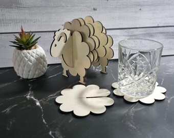 May include: A wooden sheep-shaped drink coaster set with a matching sheep figurine and a glass. The coasters are flower-shaped with a slot for a glass. The sheep figurine and coasters are made of light-coloured wood.