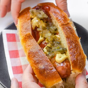 May include: A hot dog in a toasted, golden-brown bun topped with yellow mustard, red ketchup, and a generous portion of chopped green relish. The sausage is browned and nestled within the split bread, creating a classic savory food item.