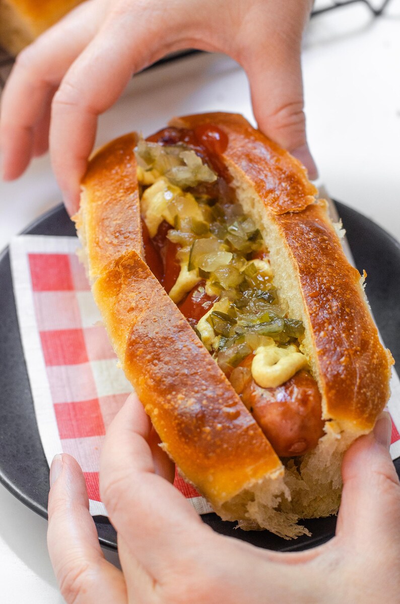 May include: A hot dog in a toasted, golden-brown bun topped with yellow mustard, red ketchup, and a generous portion of chopped green relish. The sausage is browned and nestled within the split bread, creating a classic savory food item.