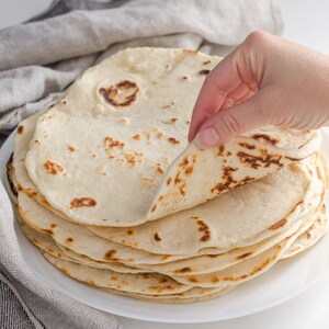 Sourdough tortillas on a plate with a hand lifting one up.