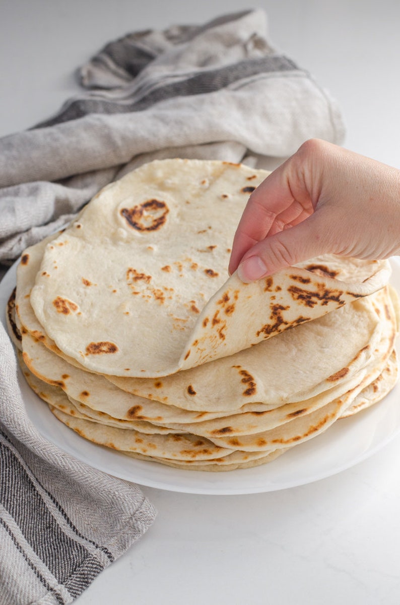 Sourdough tortillas on a plate with a hand lifting one up.