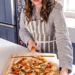 A woman holding a pizza peel with sourdough pizza on it.
