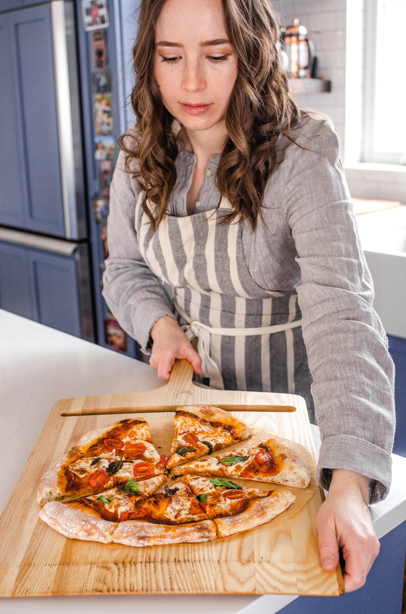 A woman holding a pizza peel with sourdough pizza on it.