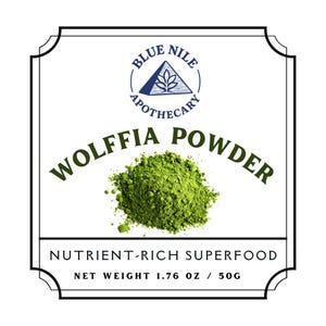 May include: A white label with a black border features the text "BLUE NILE APOTHECARY" and "WOLFFIA POWDER". A pile of green powder is in the center. The text "NUTRIENT-RICH SUPERFOOD" and "NET WEIGHT 1.76 OZ / 50G" are also present.