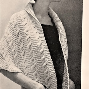 May include: A white knitted cardigan with a cable knit pattern and two large pockets. The cardigan is open in the front and has a shawl collar.