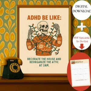 Könnte beinhalten: Ein gerahmter Druck mit dem Text "ADHD BE LIKE:" und einer Illustration eines Skeletts, das einen Pullover und Lichterketten trägt. Der Druck sagt auch "DECORATE THE HOUSE AND REORGANIZE THE ATTIC AT 2AM." Ein Vintage-Telefon steht auf einer Holzoberfläche.