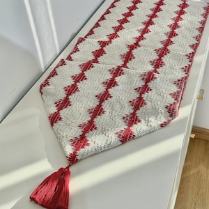 Puede incluir: Camino de mesa con estampado blanco y rojo con diseño de diamantes. El camino de mesa tiene un aspecto texturizado y está adornado con borlas rojas en un extremo. El camino de mesa mide aproximadamente 152 cm de largo.