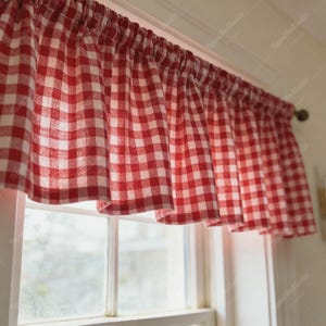 May include: A red and white checkered valance curtain hangs above a window. The fabric is gathered at the top, creating soft folds. The window treatment adds a touch of country charm to the room.