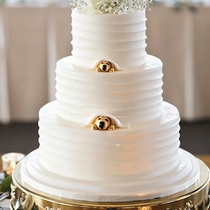 Può includere: Una torta bianca a tre piani con glassa a righe orizzontali, decorata con fiori bianchi e nebbiolina. Due piccole statuine di cani dorati spuntano dai bordi inferiori del piano superiore e di quello centrale.