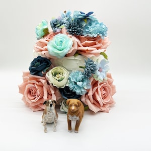 Peut inclure: Un g&acirc;teau d&eacute;coratif orn&eacute; de roses couleur p&ecirc;che, de fleurs turquoise et bleues. Deux petites figurines de chiens sont plac&eacute;es devant le g&acirc;teau. Le g&acirc;teau est blanc avec un arrangement floral.