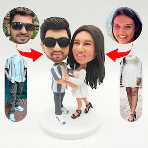 May include: A custom-made figurine of a couple embracing, with oversized heads and detailed facial features. The male figure wears a striped shirt and sunglasses, while the female figure is in a white dress. The base is white, and the overall design is whimsical.