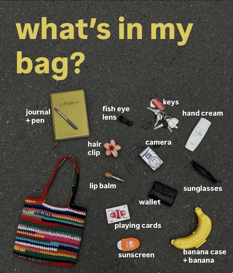 May include: A collection of everyday essentials, including a journal, pen, fish eye lens, keys, hand cream, camera, sunglasses, wallet, playing cards, sunscreen, banana case with banana, and a colourful crocheted bag. The text "what's in my bag?" is at the top.