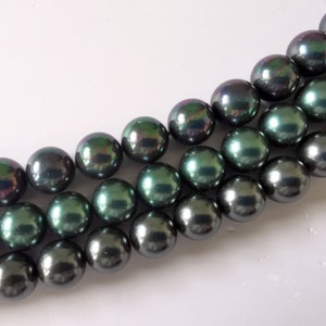 May include: A strand of dark green and black iridescent pearls. The pearls are round and smooth, and they have a high lustre.