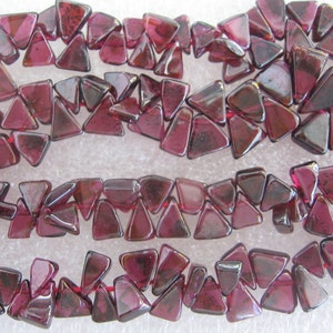 Puede incluir: Una hebra de cuentas de piedras preciosas triangulares de color rojo intenso. Las cuentas son facetadas y tienen un acabado brillante.