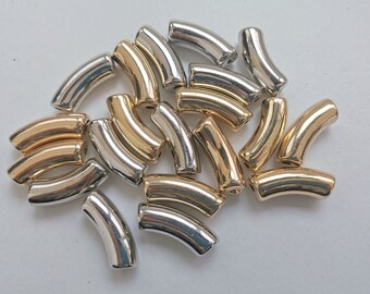May include: A collection of gold and silver metal beads in a curved shape. The beads are arranged in a pile on a white surface.