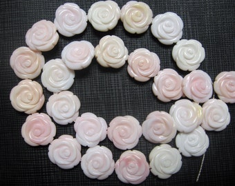 Könnte beinhalten: Eine Kette aus rosa und weißen Muschelrosenperlen. Die Perlen sind in Form von Rosen geschnitzt und haben eine glänzende Oberfläche.