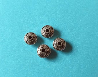 Könnte beinhalten: Vier silberfarbene, runde Perlen mit aufwendigen geätzten Designs. Jede Perle hat ein zentrales Loch und ein detailliertes Muster an den Rändern. Die Perlen sind auf einem helltürkisen Hintergrund angeordnet.