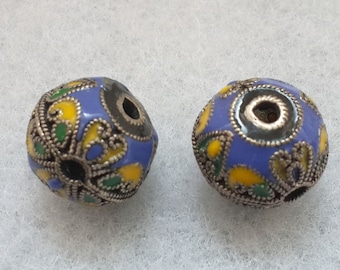 Könnte beinhalten: Zwei runde Perlen mit aufwendigen Designs. Die Perlen sind blau mit gelben, grünen und schwarzen Akzenten. Die Perlen haben einen silbernen Rand und ein Loch in der Mitte.