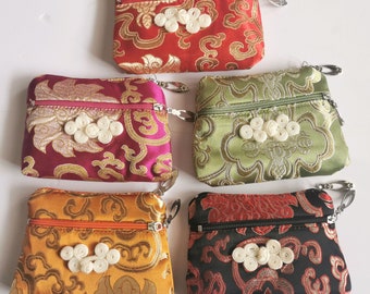 May include: Five small zippered pouches with different floral patterns. Each pouch has a white button detail and a silver zipper pull. The pouches are made of a brocade fabric and are available in red, green, yellow, black, and pink.