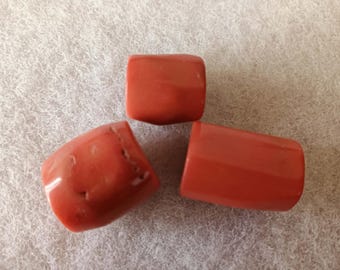 Könnte beinhalten: Drei polierte, rechteckige Korallenperlen in verschiedenen Ausrichtungen. Die Perlen haben eine leuchtende rot-orange Farbe mit glatten, abgerundeten Kanten. Die Perlen werden auf einer strukturierten, cremefarbenen Oberfläche präsentiert.
