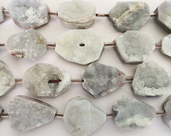 Könnte beinhalten: Eine Kette aus hellgrauen, unregelmäßig geformten Kristallperlen mit einer natürlichen, rauen Textur. Die Perlen sind auf silbernem Draht aufgefädelt.