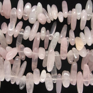 May include: A close-up of a strand of pink rose quartz beads. The beads are smooth and polished, and they have a natural, irregular shape. The beads are strung on a clear thread.