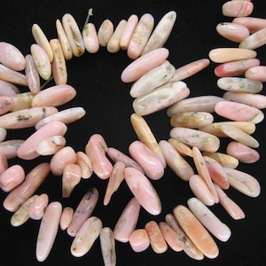 May include: A strand of pink and white opal beads, each bead is a long, thin oval shape.