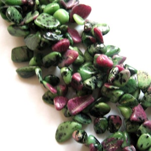 Könnte beinhalten: Eine Strähne aus grünen und rosafarbenen Edelsteinperlen. Die Perlen sind unregelmäßig geformt und haben ein gesprenkeltes Muster.