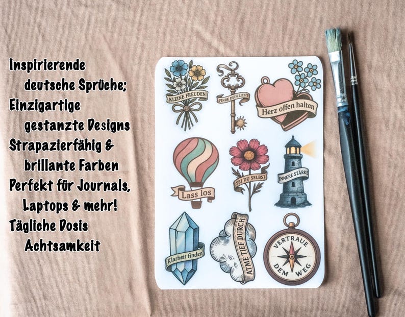 May include: A sheet of stickers with various designs, including a hot air balloon, a lighthouse, a compass, and floral elements. The stickers have German text and are accompanied by two paintbrushes.