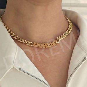 Puede incluir: Un collar de cadena dorada con un colgante de placa que dice "DOREMI".