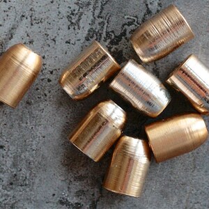 May include: A group of eight gold and silver bullet casings. The casings are arranged in a cluster on a grey textured surface.