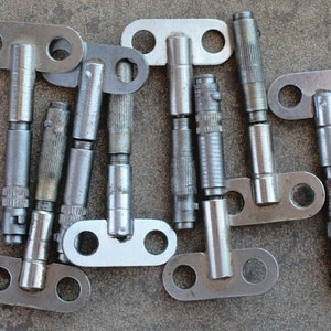 Puede incluir: Un grupo de llaves de metal plateadas con un mango en forma de T y un agujero redondo a cada lado. Las llaves están dispuestas en un patrón aleatorio sobre una superficie gris texturizada.