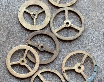 May include: Seven antique brass gears with three spokes each, arranged on a grey surface.