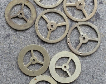 May include: Eight antique brass clock gears, each with three spokes, arranged in a semi-circle on a grey textured surface.