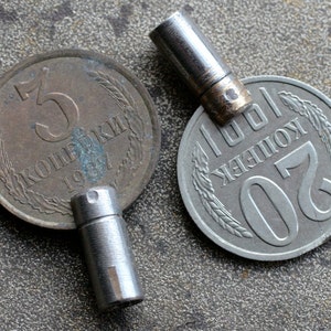 以下が含まれることがあります： 「3 копейки 1974」と「20 копеек」の文字が刻まれた、2つのビンテージのソビエトコインが、金属製のキーホルダーに取り付けられています。