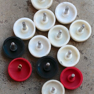 Könnte beinhalten: Eine Sammlung von 12 runden, weißen, schwarzen und roten Knöpfen mit einem Metallstift in der Mitte. Die Knöpfe sind in einem Kreis auf einer grauen Oberfläche angeordnet.