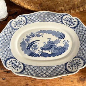 May include: Oval serving platter with a white and blue floral design. The platter features a central image of two birds and foliage, surrounded by a blue and white geometric pattern. The edges have a scalloped design.