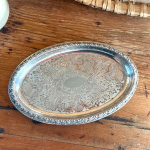 May include: Oval silver serving tray with ornate floral and scrollwork design. The tray has a detailed border and a polished, reflective surface. A classic piece for serving or display.