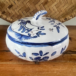 May include: A white ceramic lidded jar with blue floral and bird designs. The jar has a rounded shape with a blue rim and a curved handle on the lid. The floral pattern includes leaves and stylized flowers.