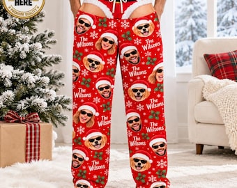 May include: Red pajama pants featuring a repeating pattern of white snowflakes, green holly leaves, and custom faces of people and dogs wearing Santa hats and sunglasses, with the text The Wilsons printed below each face and a white drawstring waist.