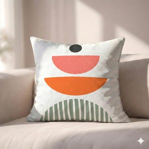 Könnte beinhalten: Quadratisches Kissen mit weißem Hintergrund und geometrischem Design. Das Design zeigt einen schwarzen Kreis, einen korallenfarbenen Halbkreis, einen orangefarbenen Halbkreis und einen grün-weiß gestreiften Halbkreis.