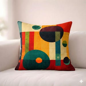 May include: Square cushion with a vibrant abstract design. The cushion features a colourful geometric pattern with circles, rectangles, and stripes in shades of red, orange, yellow, green, and blue. The cushion is on a white sofa.