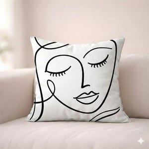 Könnte beinhalten: Quadratisches weißes Kissen mit einer minimalistischen schwarzen Strichzeichnung eines Gesichts. Das Design zeigt geschlossene Augen und volle Lippen und schafft einen modernen, künstlerischen Look. Dieses dekorative Kissen wäre ein stilvoller Akzent für ein Sofa oder Bett.