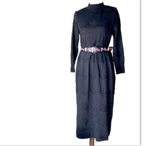 May include: A black long-sleeved dress with a textured pattern and a high neck. The dress is cinched at the waist with a black belt with a skull and rose design.