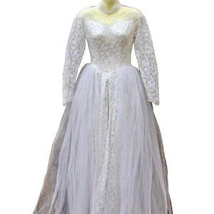 Könnte beinhalten: Ein weißes Spitzen-Hochzeitskleid mit langen Ärmeln und einem Tüllrock. Das Kleid hat ein tailliertes Oberteil und einen herzförmigen Ausschnitt.