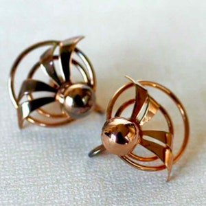 以下が含まれることがあります： 幾何学的なデザインのゴールドトーンのイヤリングのペア。イヤリングは、中央の球体と放射状の線を持つ円形の形をしています。