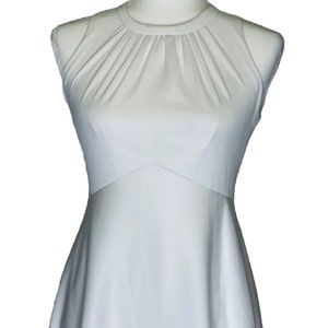 Könnte beinhalten: Ein weißes ärmelloses Kleid mit hohem Ausschnitt und einem plissierten Oberteil. Das Kleid hat ein tailliertes Oberteil und einen fließenden Rock.