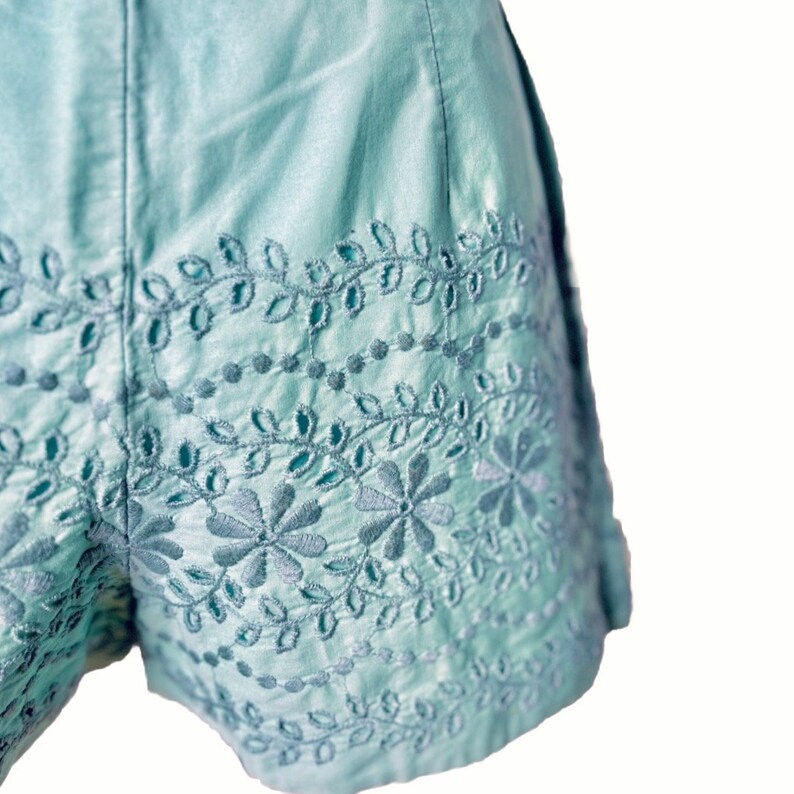 May include: Light blue embroidered shorts with a floral pattern. The shorts have a scalloped hem and a high waist.
