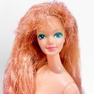 Puede incluir: Una muñeca vintage con cabello largo de color rojo anaranjado. La muñeca tiene ojos azules con sombra de ojos verde y labios rosados. El tono de piel de la muñeca es claro, y la imagen es un primer plano de la cara y la parte superior del cuerpo de la muñeca.